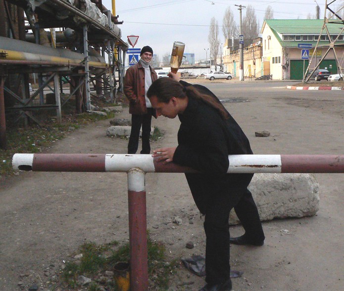 Варшавский пытаеца бутылкой шампанского забить гвоздь в железной трубе.